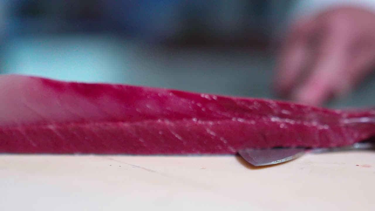 Watch a close-up shot of a tuna fish being expertly skinned, highlighting the skill and technique involved in preparing this fresh fish for further culinary use.
