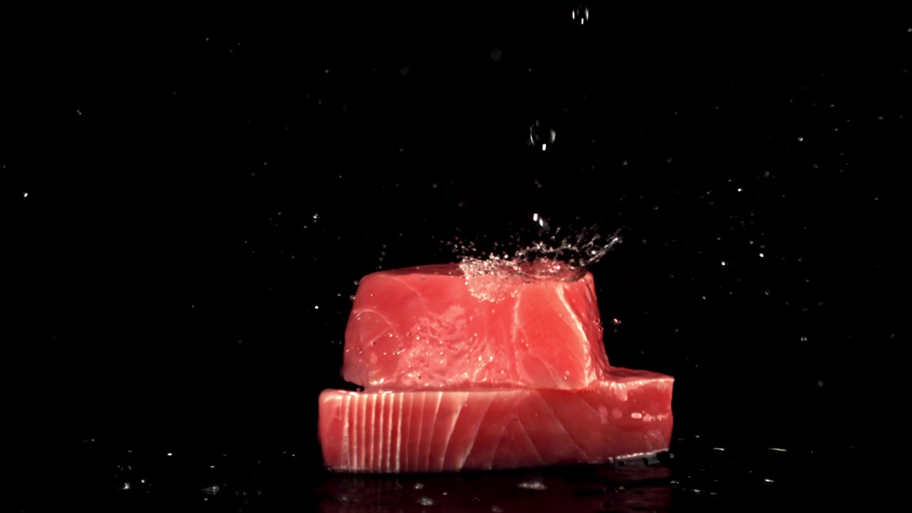 Gocce d'acqua al rallentatore che schizzano su tranci di tonno fresco crudo