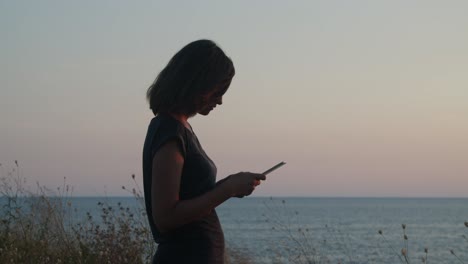 Mädchen,-Das-Bei-Sonnenuntergang-Auf-Einer-Klippe-Am-Meer-Steht---Goldene-Stunde,-Mit-Tablet-Computer-In-Der-Nähe