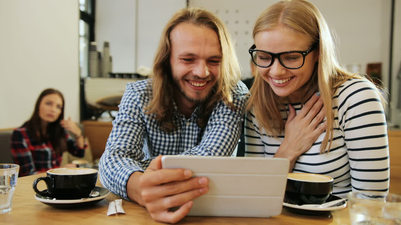 vista de cerca de amigos caucásicos felices riéndose y viendo un video en una tableta sentados en una mesa en un café