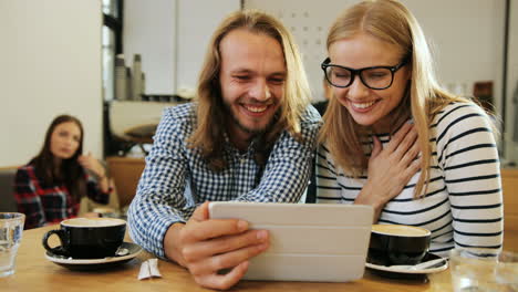 close-up view of caucasian happy friends laughing and watching a video on a tablet sitting at a table in a cafe