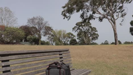 Small-grey-blue-camera-bag-left-in-the-middle-of-a-wooden-park-bench