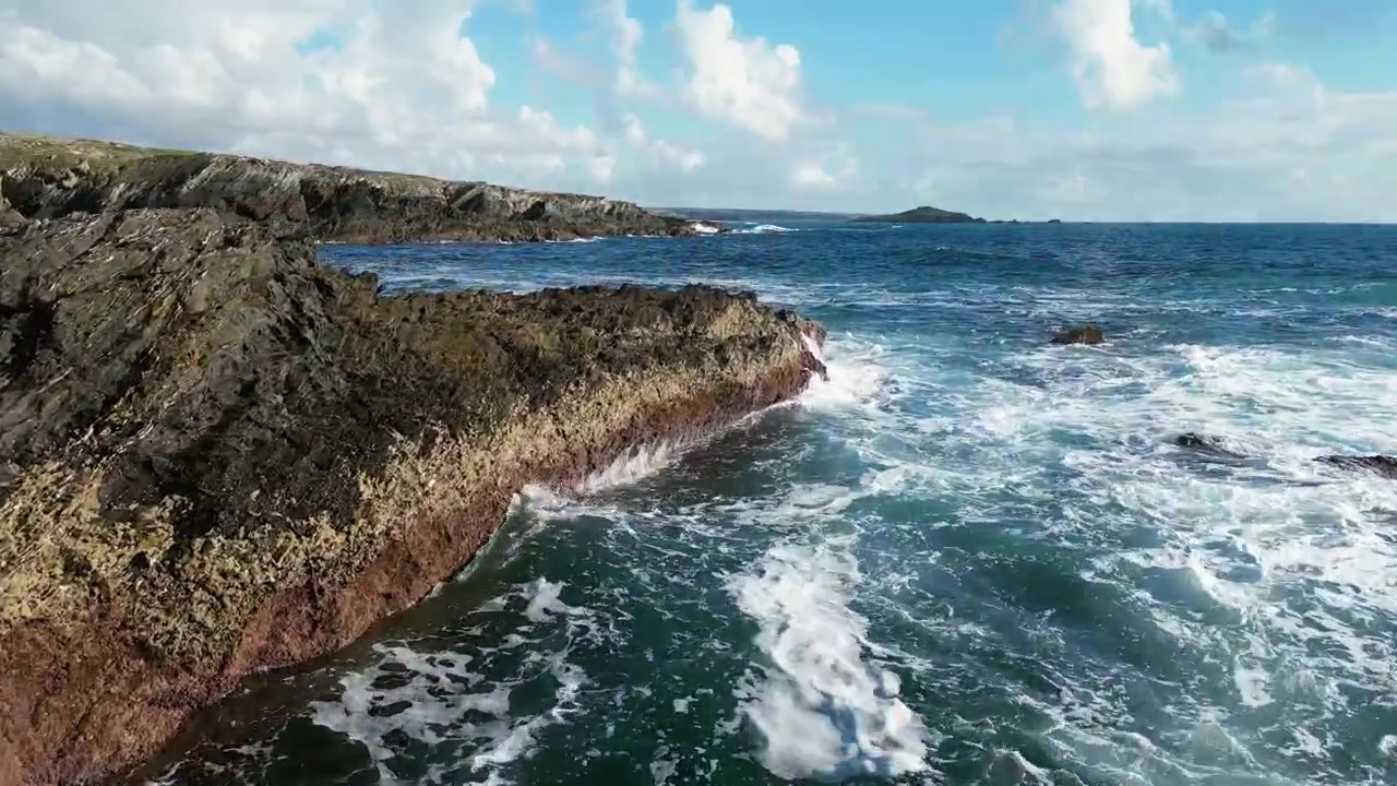 Rekaman drone udara Praia dos Buizinhos, Portugal: tebing Atlantik yang terjal, ombak laut, dan pemandangan pantai alami di bawah cahaya matahari. Ideal untuk proyek perjalanan dan alam