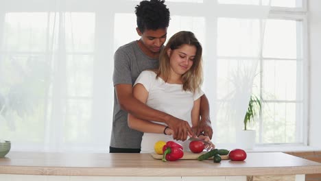 Un-Apuesto-Hombre-Africano-Está-Abrazando-A-Una-Novia-Caucásica-Mientras-La-Ayuda-A-Preparar-Comida-En-La-Cocina-Por-La-Mañana.-Feliz