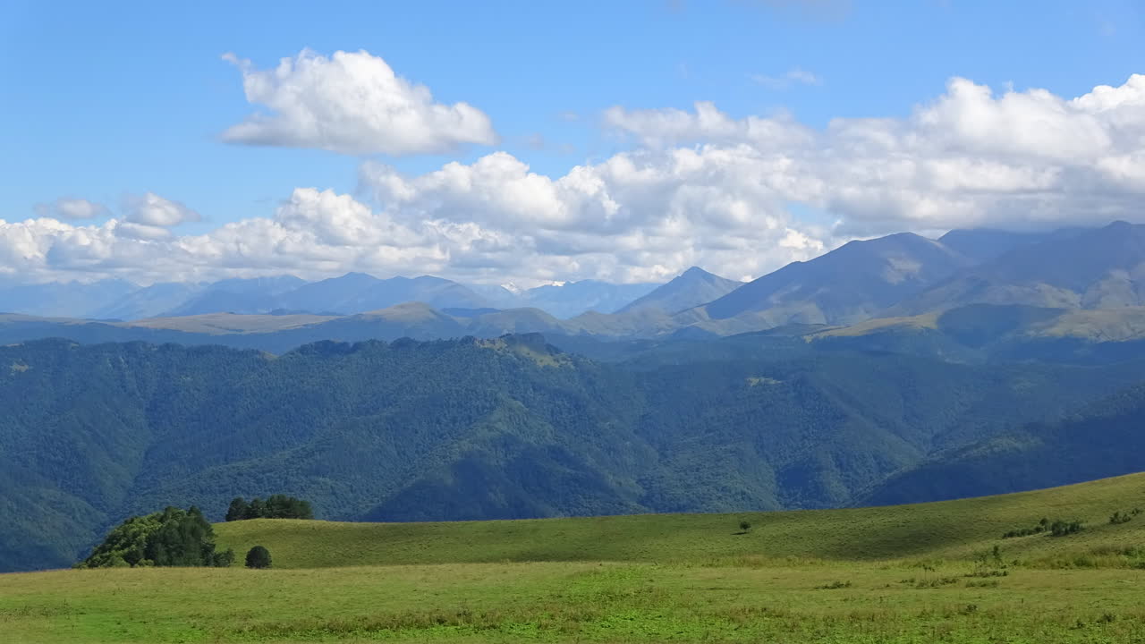 森林に覆われた尾根と緑豊かな高山牧草地の上を雲が漂う、広大なカフカス山脈のパノラマのタイムラプス映像。美しい自然の背景。
