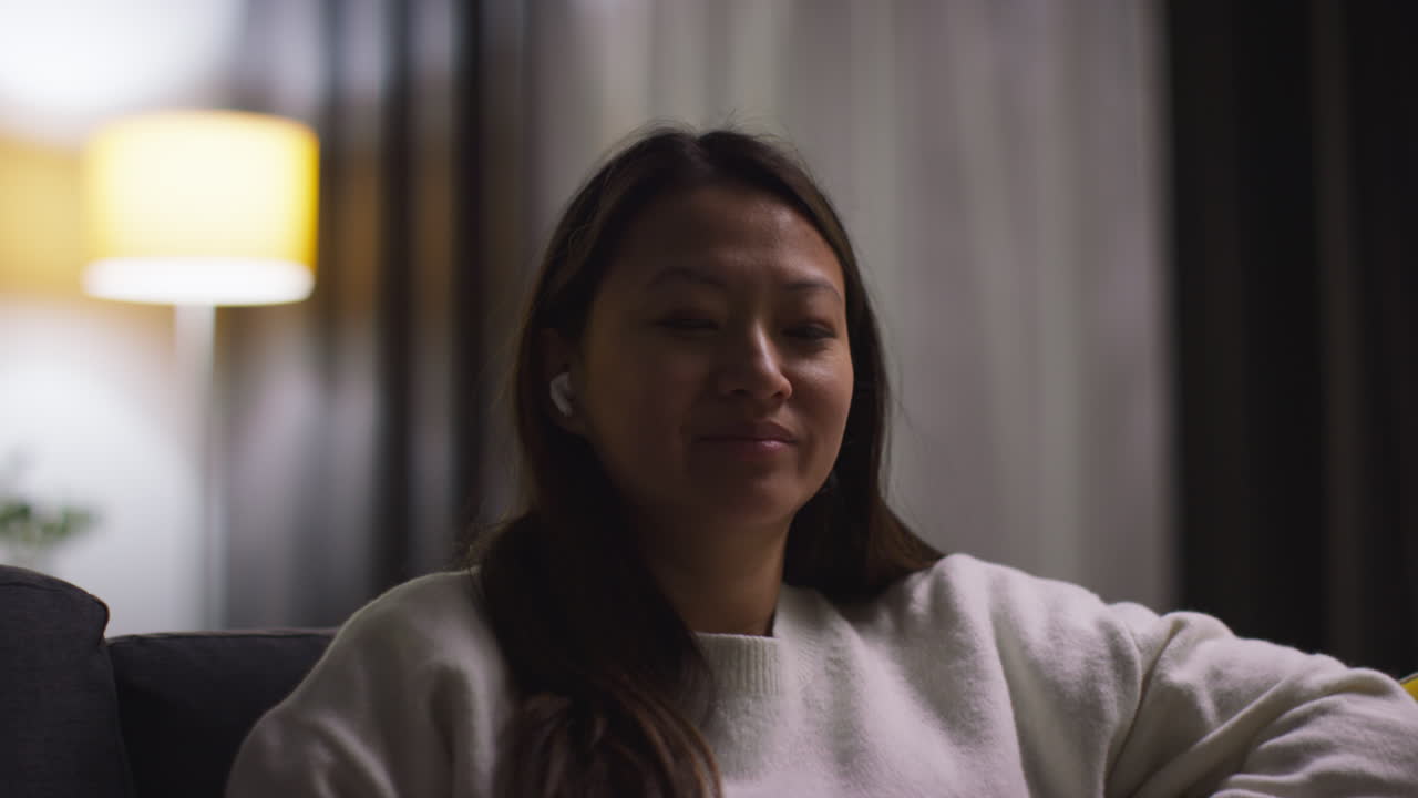 소파에서 집에서 저녁을 보내고 무선 이어을 착용하고 휴대 전화 4에서 음악이나 캐스트를 스트리밍하는 여성의 클로즈업