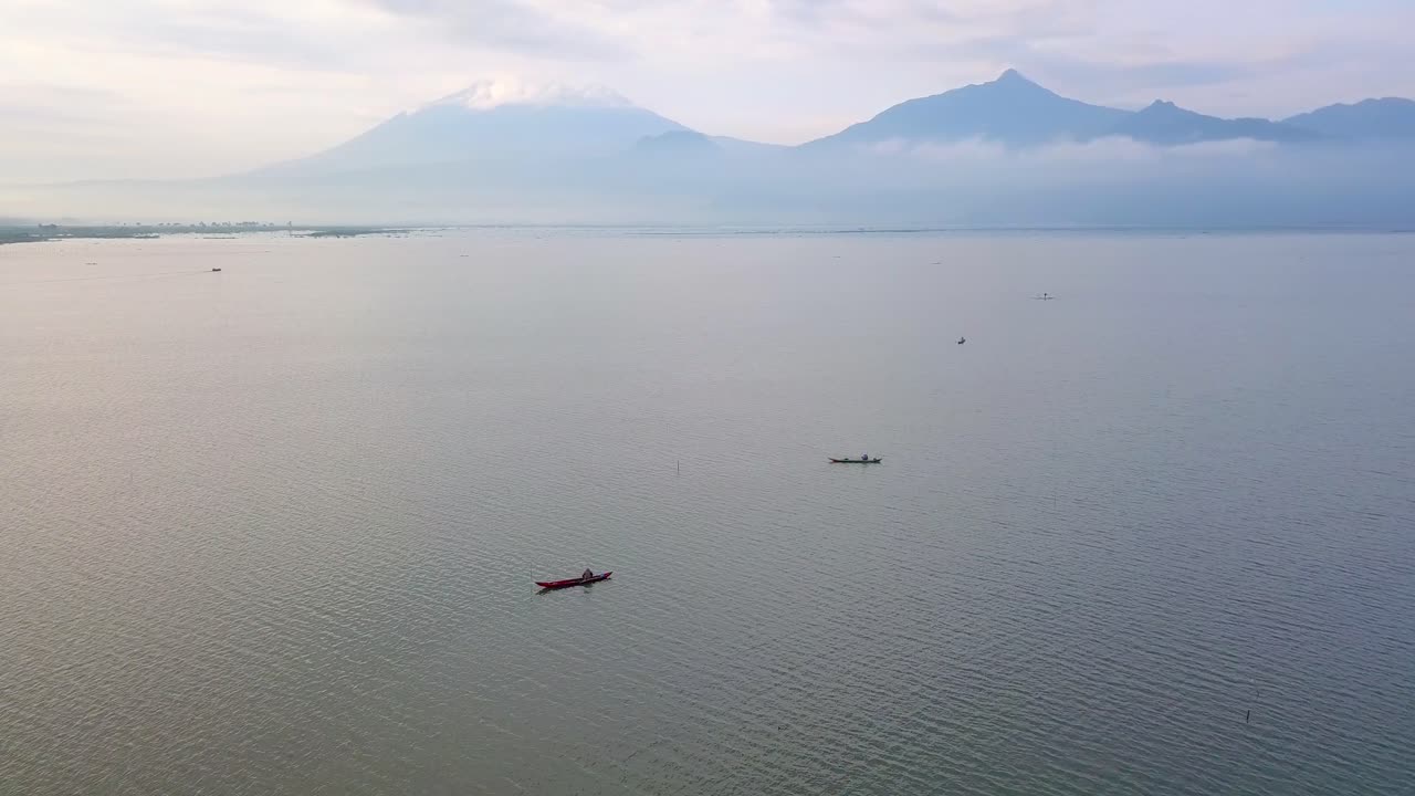 toma de un dron en órbita de un barco tradicional de madera en el enorme lago con una montaña al fondo - lago rawa pening, indonesia