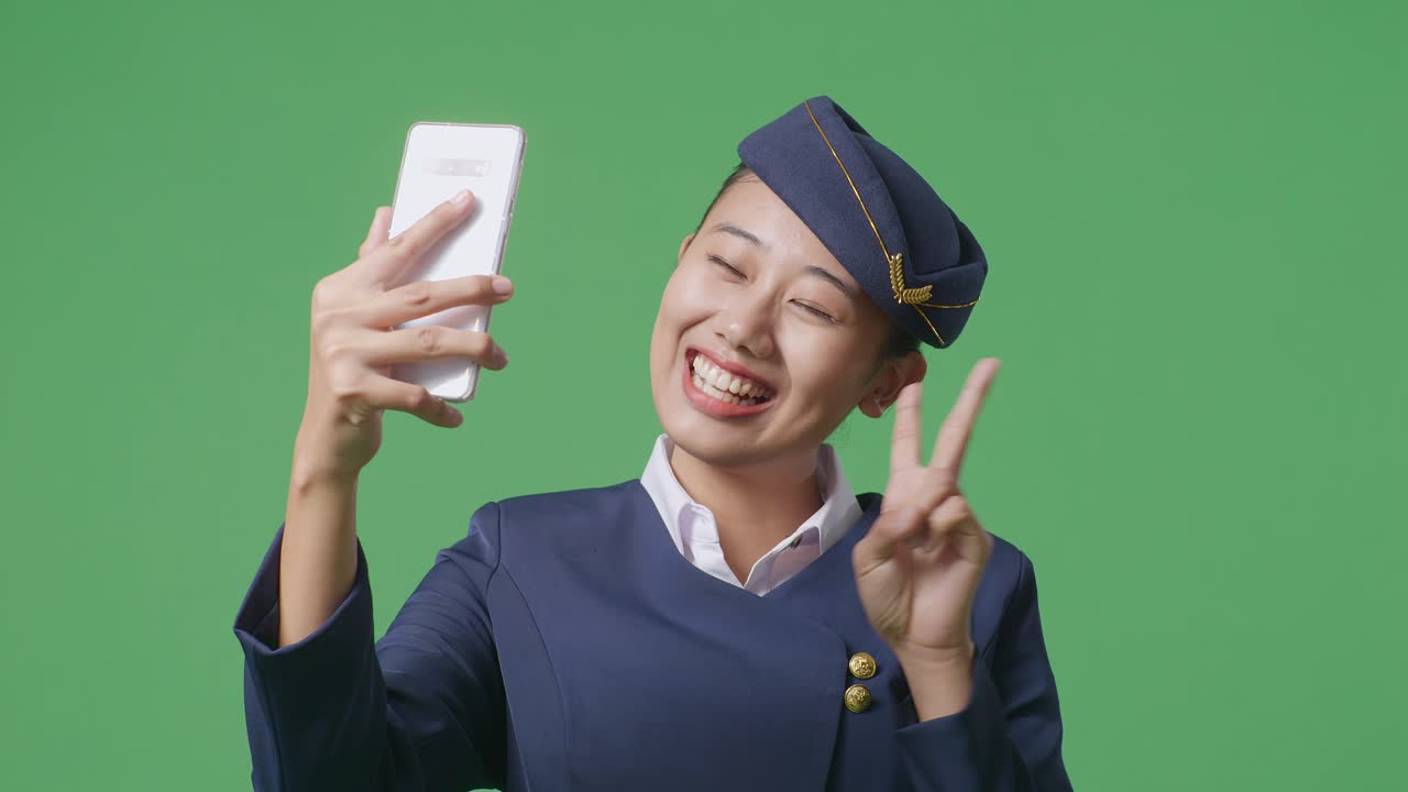 녹색 스크린 배경 스튜디오에 서서 사진을 찍는 스마트폰을 사용하는 아시아 여성 에어 호스테이스의 클로즈업
