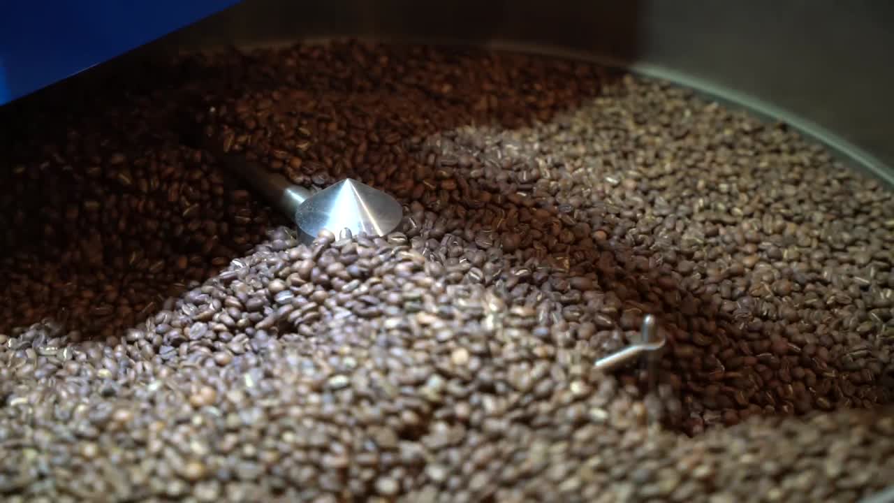 Coffee bean roaster machine strongly mixing and turning the grains with steel arms, Handheld close up shot