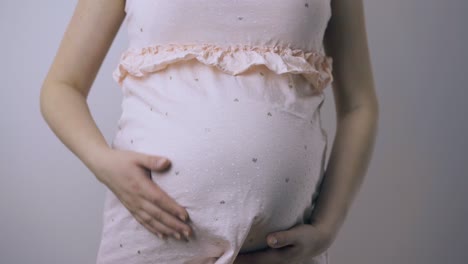 pregnant lady strokes large tummy with hands at wall closeup