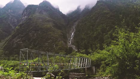 Puente-De-Metal-Nepalí-Rodeado-De-Montañas-Con-Una-Cascada---Langtang-Trek,-Nepal