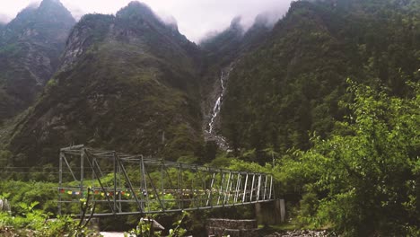 puente de metal nepalí rodeado de montañas con una cascada - langtang trek, nepal