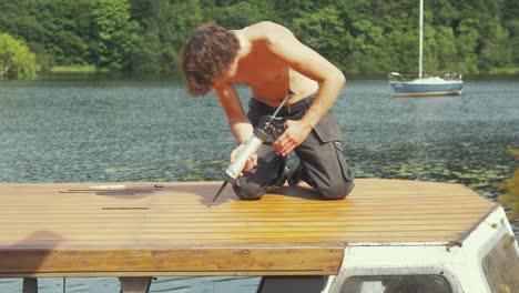 boat maintenance, young man seals roof planking of old wooden boat in summer