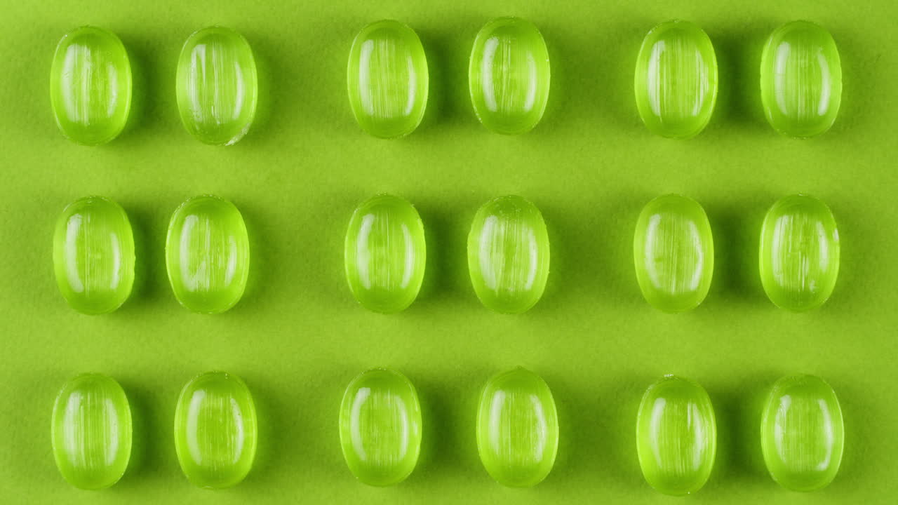 Green mint mentol lollipops, candies, bonbons disappear on purple background. Summer bright texture studio shot for store, supermarket, close up top view. Children favorite sweets made of sugar.