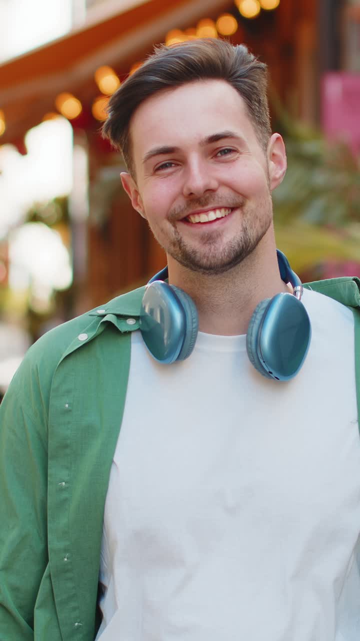 Portrait of smiling young male tourist in casual clothes with wireless headphones around neck