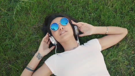 mujer relajándose en la hierba con auriculares y gafas de sol