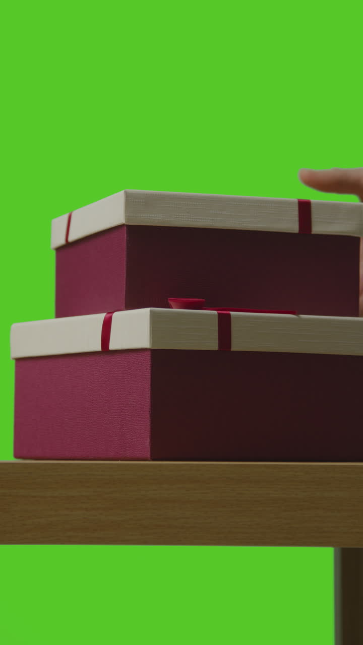 video vertical de un hombre recogiendo pilas de regalos en cajas envueltas en regalos de una mesa disparada contra una pantalla verde