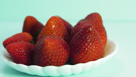 fresh big red tasty ripe strawberries rotates slowly on a white plate on light blue background, healthy food concept, medium close up shot, camera rotate right