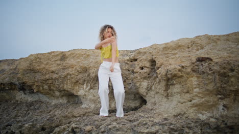 curly girl performer dancing on sandy rock at summer evening. woman moving body