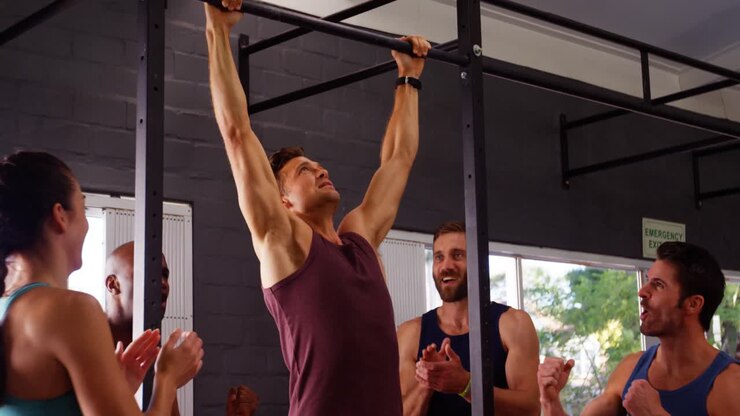 Men performing pull-up exercise while friends applauding him