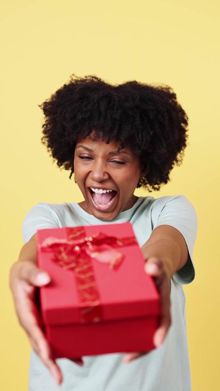 Donna afroamericana allegra che offre una scatola regalo rossa alla fotocamera