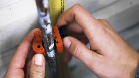 male hands twist a pipecutter around a burst copper pipe