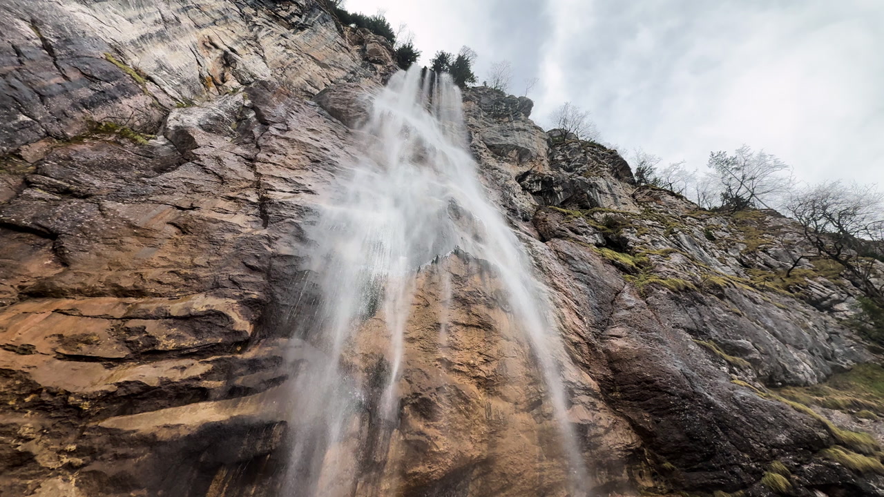 Dramatic low-angle drone shot of Skakavac waterfall cascading down high rocky cliff near Sarajevo, Bosnia and Herzegovina.