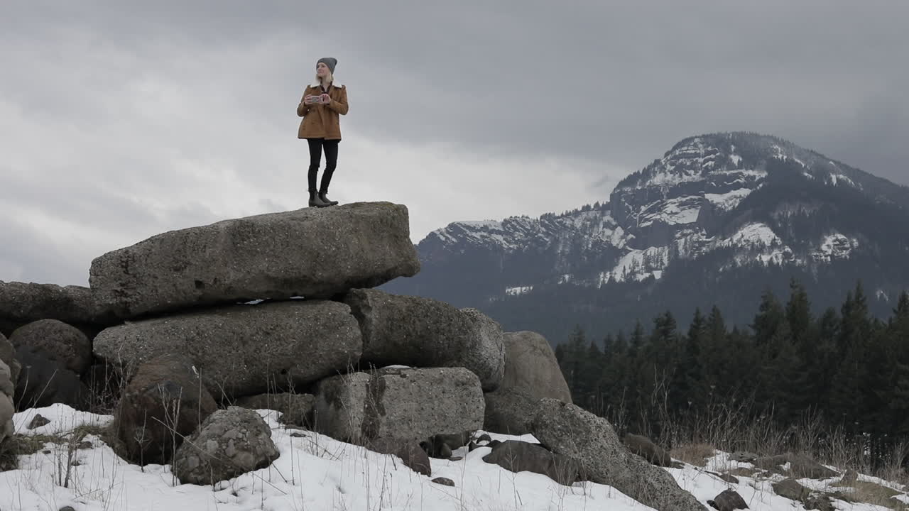 A girl takes pictures of the snowy mountains around her.