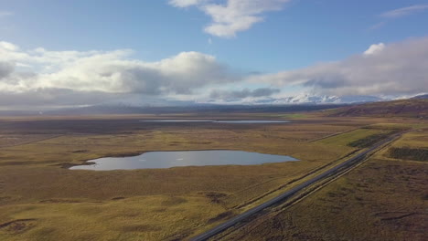 Vista-De-Drones-De-Autos-Conduciendo-Por-La-Carretera-Con-Campos,-Agua-Y-Montañas-En-La-Distancia