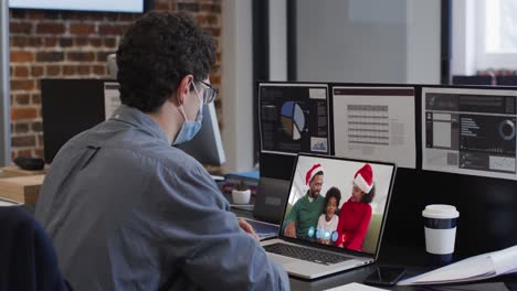 Caucasian-man-wearing-face-mask-on-video-chat-at-christmas-in-office