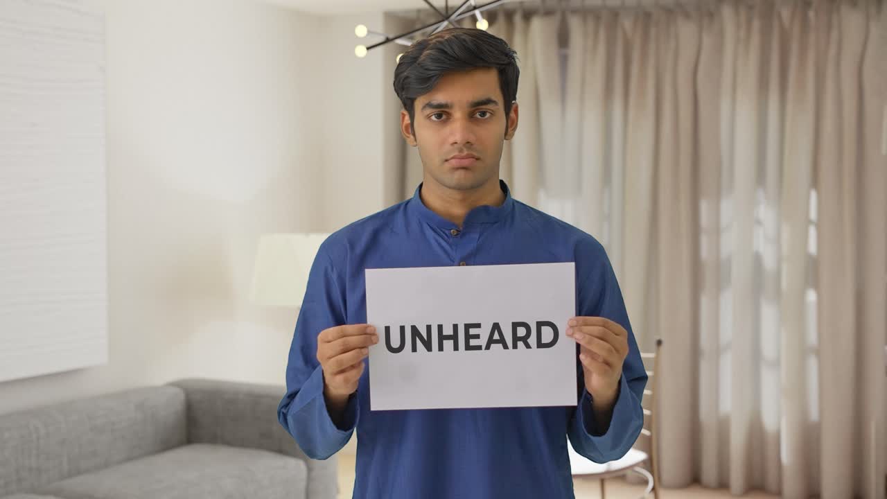Sad Indian boy holding UNHEARD banner
