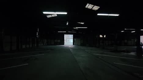 una toma cinematográfica moviéndose más profundamente en una oscura estructura de estacionamiento abandonada, más cerca de una puerta iluminada hacia el exterior