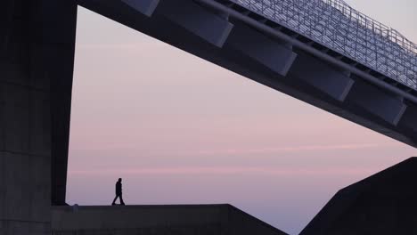 man with scooter admires purple sunrise in parc del forum, barcelona, wide shot