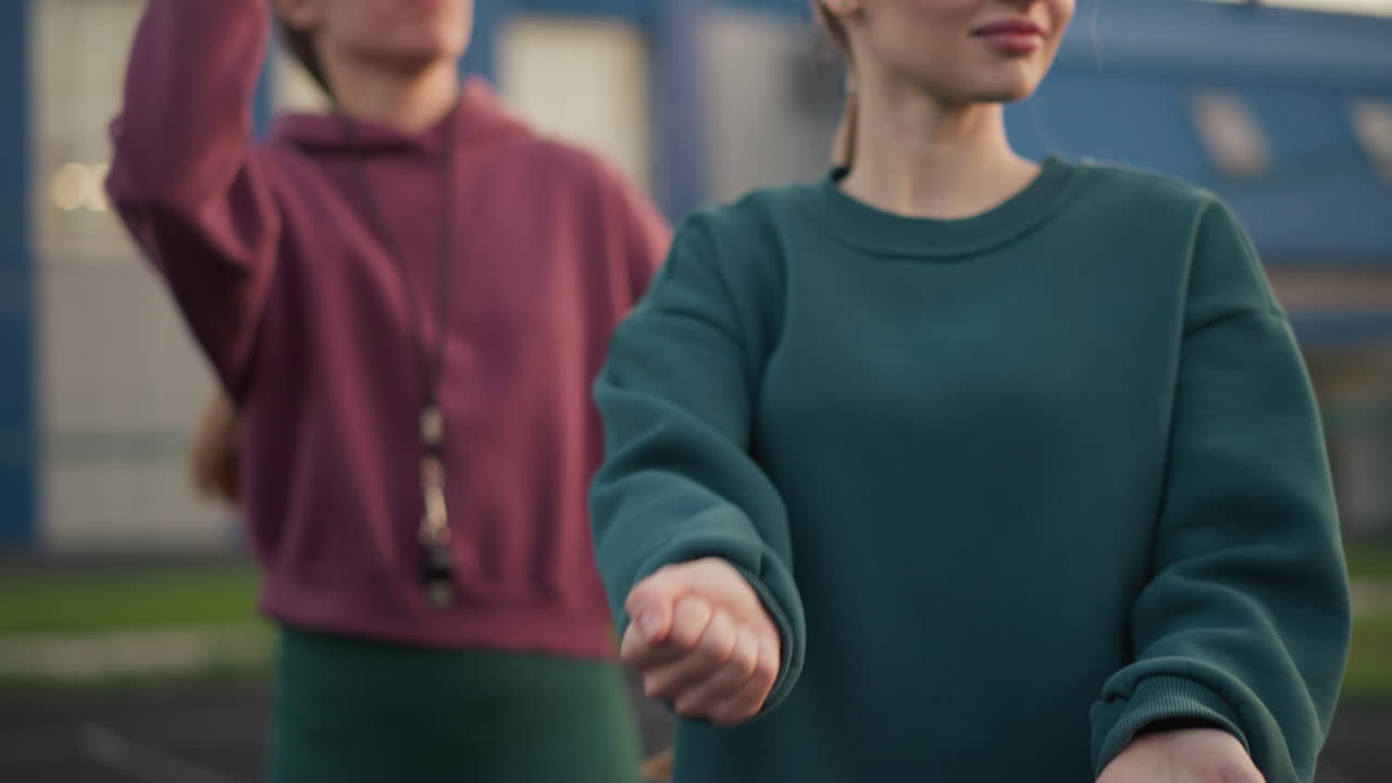 배구 초보자를 훈련시키는 코치, 초보자 연습으로 서브 기법을 보여주는 코치, 둘 다 배경에 건물과 함께 배구 공원을 들고 야외 코트에서 서 있습니다.