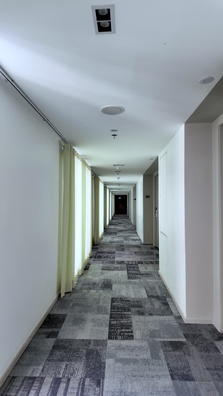 Long hotel corridor with left curtains, patterned carpet, and distant dark end, suggesting calm, empty space