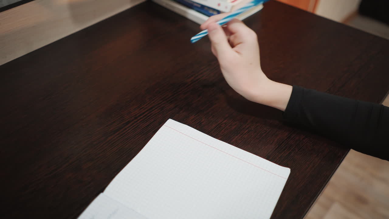 Scena di scrittura su quaderno. Scrivania scura con appunti manoscritti. Una persona prende appunti alla scrivania con un'illuminazione interna accogliente. Scrittura a mano su quaderno, su una scrivania scura con libri e in un ambiente sereno.