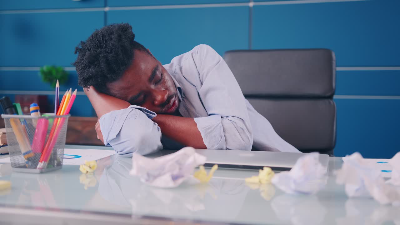 Giovane impiegato afroamericano stanco che dorme alla scrivania