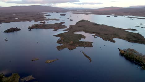 Eine-Drohne-Fliegt-Langsam-Hoch-über-Einer-Patchwork-Landschaft-Aus-Inseln,-Die-Mit-Bäumen-übersät-Sind-Und-Zwischen-Süßwasserseen-Liegen-Und-Bei-Sonnenuntergang-Von-Torfmooren-Umgeben-Sind