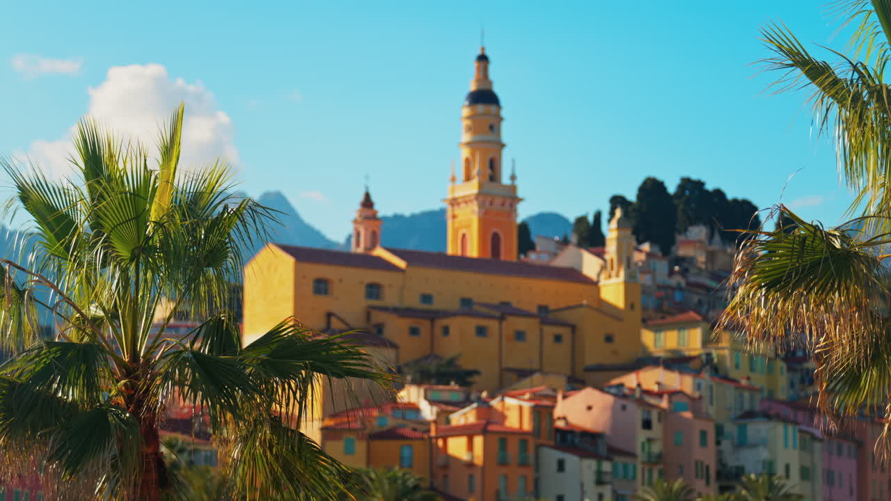 Distant view of the St Michel Basilica surrounded by colourful buildings and palm trees, Menton, France