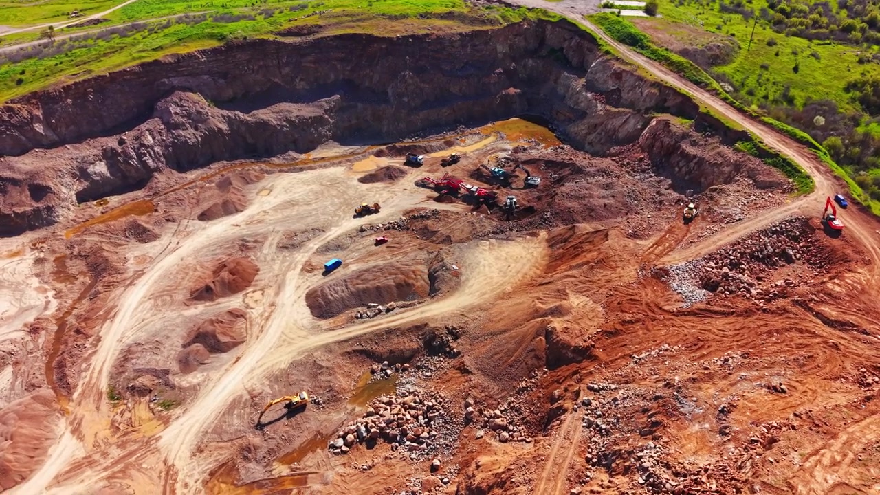 Deep excavation layers, dirt tracks, mining equipment and loose stone mounds. High angle view of deep open pit rock quarry, Bulgaria.