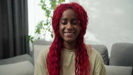 retrato de una mujer afroamericana sonriente con cabello rojo elegante en casa, mirando a la cámara y riendo