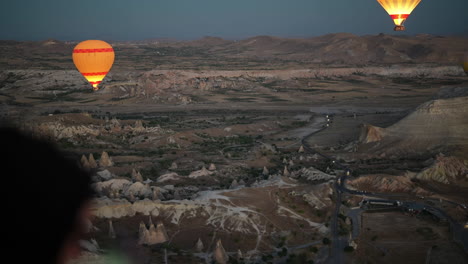 aerial pov of cappadocia at dawn from hot air balloon, burners and parachutes above scenic landscape