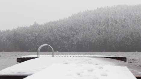 snow falling on alta lake with water rippling and docking deck swaying against coniferous evergreen forest mountain covered in white snow, beautiful winter scene