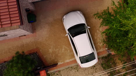 antena de arriba hacia abajo del coche sedán blanco entrando en el garaje para aparcar en casa