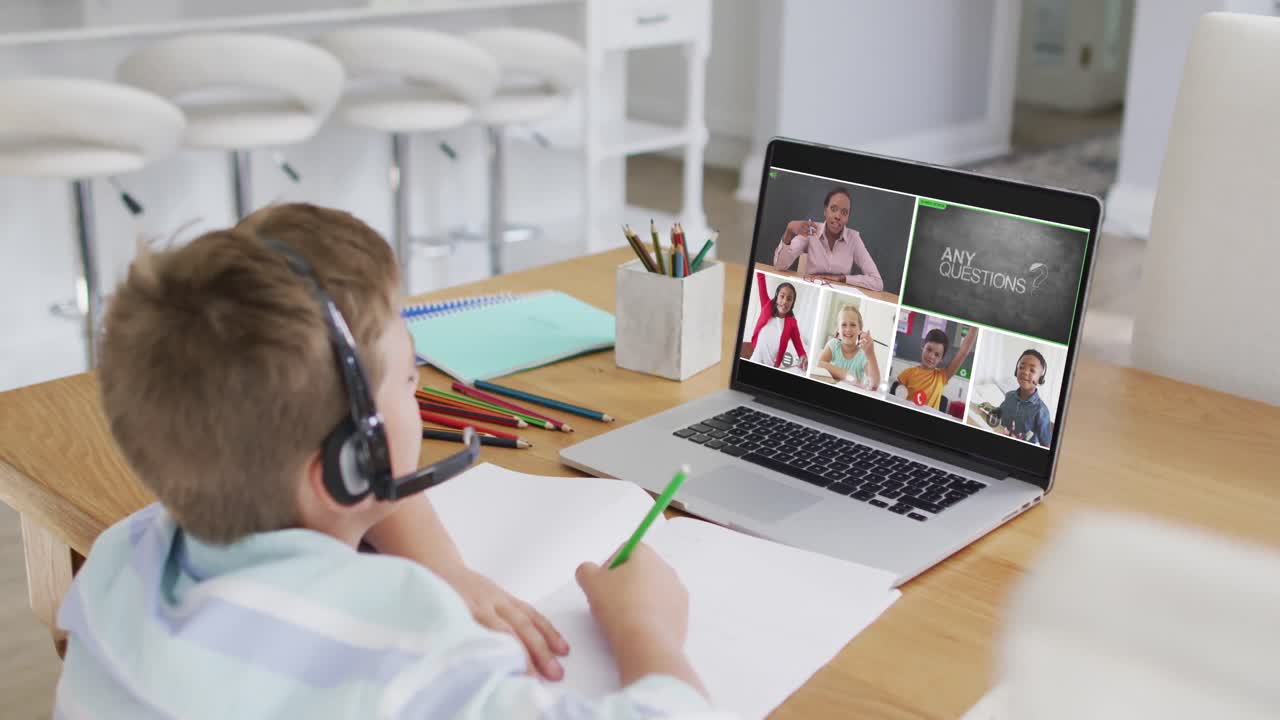 Schoolboy using laptop for online lesson at home, with diverse teacher and class on screen