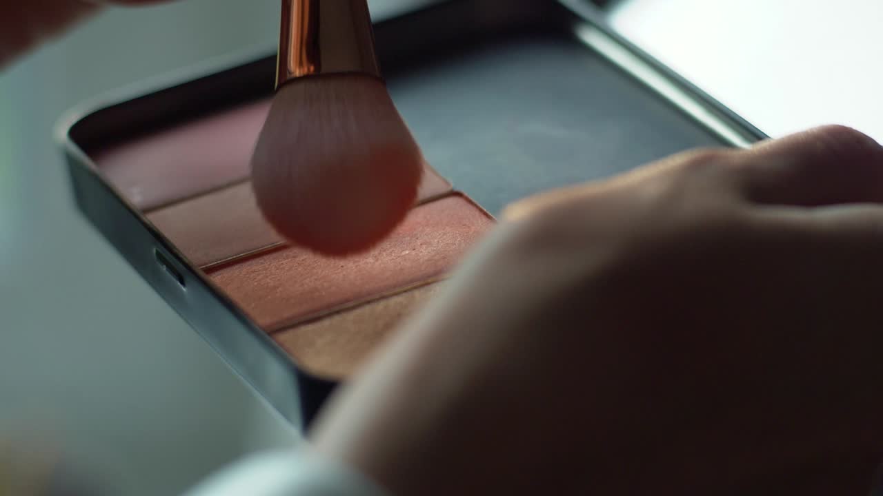 Soft brush wipes packs of color in makeup pallet to be applied to face of customer in salon. Wedding and beauty pageant preparation concept. Cosmetic application technique and product.