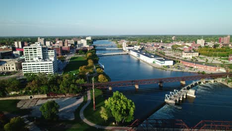 una toma aérea del centro de rockford, illinois, revela un cautivador paisaje urbano, donde los edificios modernos se mezclan armoniosamente con exuberantes espacios verdes bordeados por el flujo sereno de un majestuoso río