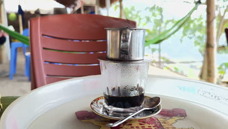 vietnamese phin filter coffee on a tray at an outdoor cafe in vietnam. relaxing scene with a hammock in the background, perfect for a tranquil coffee break.