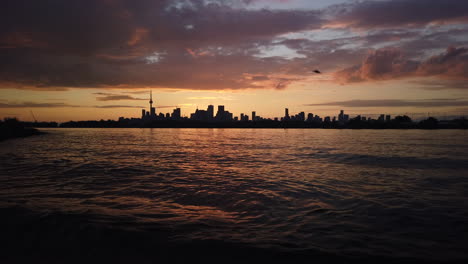 wide shot of toronto skyline and lake ontario silhouetted against a twilight sky and multi coloured clouds