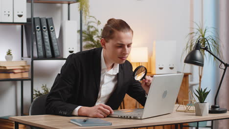 surprised researcher businessman working at home office holding magnifying glass looking at laptop